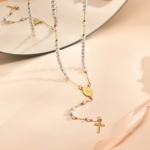 Detail view of gold Virgin Mary and cross pendant on a white pearl beaded necklace