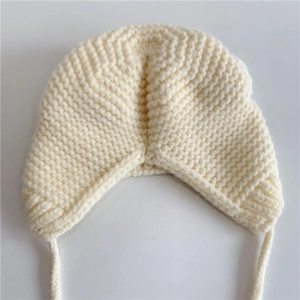 Detail of cream white knit baby winter hat with cute ear flaps and visible knit texture