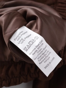 Detailaufnahme des Pflegeetiketts und des Innenfutters aus 100% Polyester der braunen Jacke