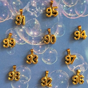 Gold 90s birth year number pendants for necklaces on textured blue water background