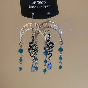 Close-up of gothic moon and snake earrings with blue crystal beads on black display card