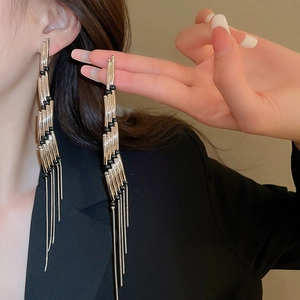 Detailed view of long tassel drop earrings with metal rods and black beads on a model