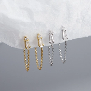 Close-up of gold and silver tassel chain earrings with inlaid gems on textured paper