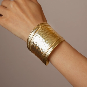 Close-up of golden wide hammered metal cuff bracelet with dotted edge on woman's wrist