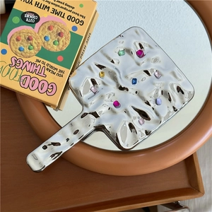 Detail of silver handheld mirror featuring water ripple texture and colorful gemstones