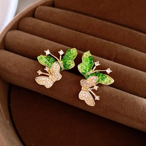 Golden butterfly earrings with green stones and white cubic zirconia on brown velvet