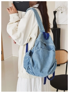 Detailed side view of blue denim backpack with dark blue straps on a model in home setting