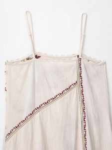 Detailed close-up of delicate lace trim and floral embroidery on cream cotton dress