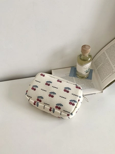 Close-up of beige canvas makeup bag with red cherry prints and Les Grenades text