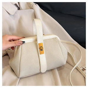 Close-up of beige shell bag featuring suede patchwork and a gold twist-lock closure