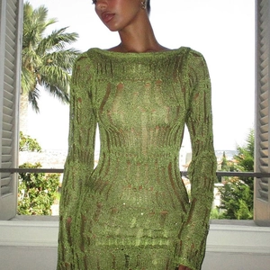 Detail of green knit dress showing openwork texture and long sleeves in soft light