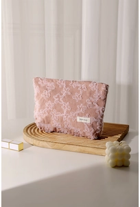 Detail view of pink corduroy makeup bag with 3D floral lace embroidery on a wooden tray