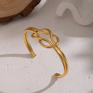 Detailed view of gold knotted cuff bracelet on a white textured background