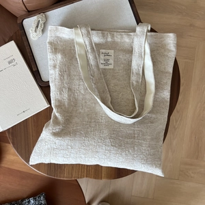 Neutral cotton linen tote bag with artistic embroidery label on dark wood table