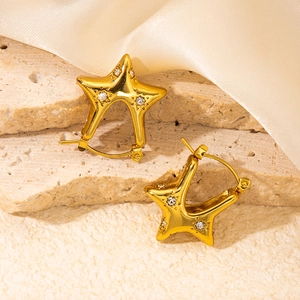 Polished gold star hoop earrings with crystal zircon insets on stone background