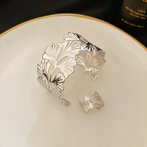 Detailed macro of silver ginkgo leaf cuff bracelet and ring set on an elegant ceramic plate