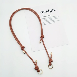 Detail of adjustable brown leather bag strap with gold metal ring and decorative knot
