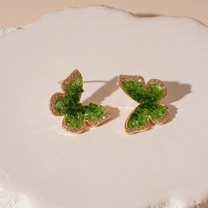 Detailed macro shot of butterfly stud earrings with green zircon and gold plating