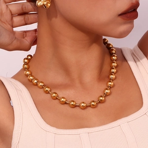Gros plan d'un collier à billes dorées et d'une boucle d'oreille organique assortie