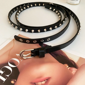 Détail d'une ceinture fine en cuir noir avec clous coniques argentés et œillets en métal