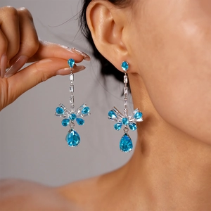 Close-up of silver bow earrings with sparkling blue teardrop zircon gemstones for women