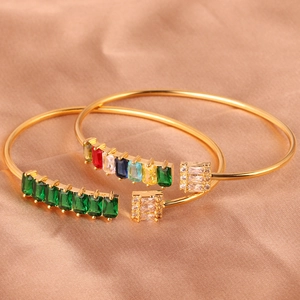 Macro-opname van gouden open armband met smaragd en veelkleurige zirkoon edelstenen
