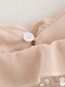 Close-up of beige chiffon fabric with white button and sparkling sequin mesh details