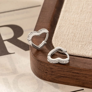 Silver heart shaped hoop earrings with cubic zirconia stones on linen background