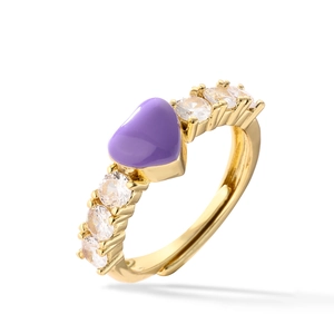 Golden heart ring with purple center stone and clear side crystals on white background