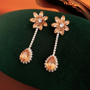 Detail of luxury teardrop champagne zircon flower earrings on dark green velvet