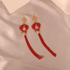 Macro shot of red fish tassel earrings with golden Chinese knots on silk fabric