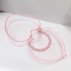 Draufsicht auf eine herzförmige transparente Box mit rosa Rand und Perlenketten-Inhalt