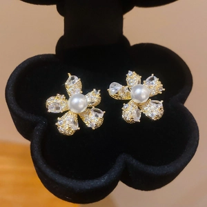 Detailaufnahme goldener Perlenohrringe mit Zirkonia-Blüten auf schwarzem Samt-Display