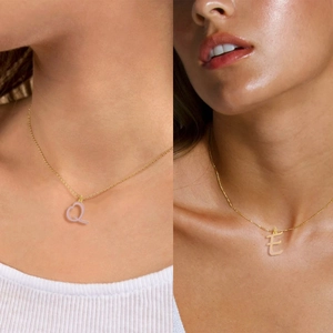 Close-up of gold necklaces featuring pink enamel letter Q and E charms on a model