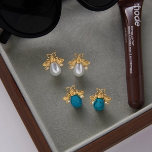 Detailed shot of bee-shaped gold earrings with pearls and turquoise on velvet