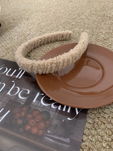 Close-up of a beige plush faux shearling headband on a brown ceramic saucer