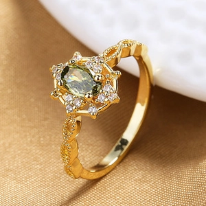 Close-up of gold leaf ring with oval green gemstone and pavé zircon accents