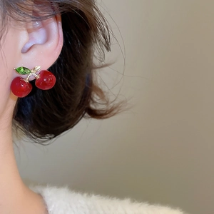 Close-up of cherry stud earrings with red resin fruit and green zircon leaves on the ear