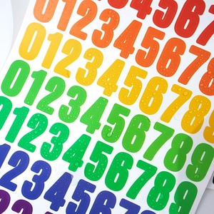 Close-up of waterproof rainbow vinyl number stickers with water droplets on white surface