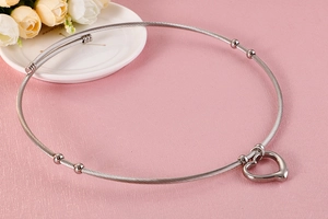 Close-up of heart-shaped pendant on silver steel wire neck collar with smooth metal beads