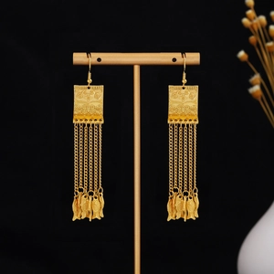 Detail of golden bohemian tassel earrings with fish pendants on a metal display stand