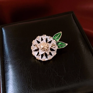 Detail of 14K gold plated flower brooch with green leaves and white zircon stones