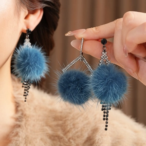 Detail of blue pompom earrings with sparkling rhinestones and chains on a model
