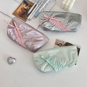 Three bow-knot stationery pencil bags in silver pink and green on a minimalist desk