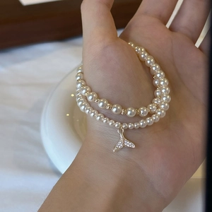 Detail of double-layer pearl bracelet featuring a gold zircon whale tail charm on a model