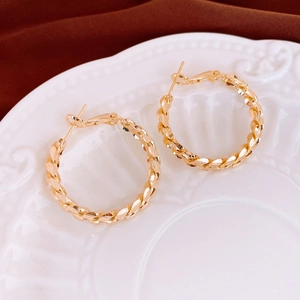 Close-up of golden twisted hoop earrings on a vintage embossed plate background