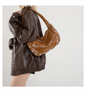 Detail of brown glossy leather crescent bag with silver studs and wide strap in Y2K style