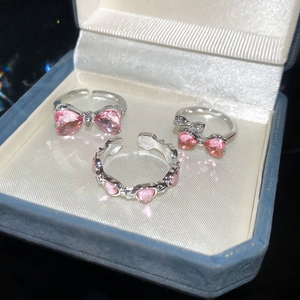 Detailed view of silver bow and heart rings with pink gems on a blue velvet jewelry box