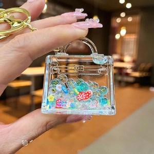 Close-up of a clear acrylic handbag charm filled with colorful beads and gold ring