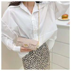 Detail of beige quilted cylindrical bag with golden chain strap and shiny patent finish